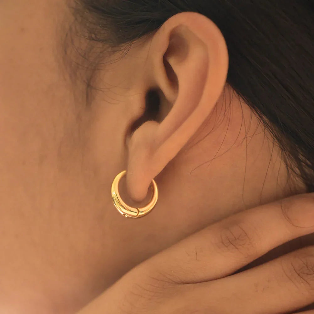 Close-up of an ear wearing a gold hoop earring with a blurred background
