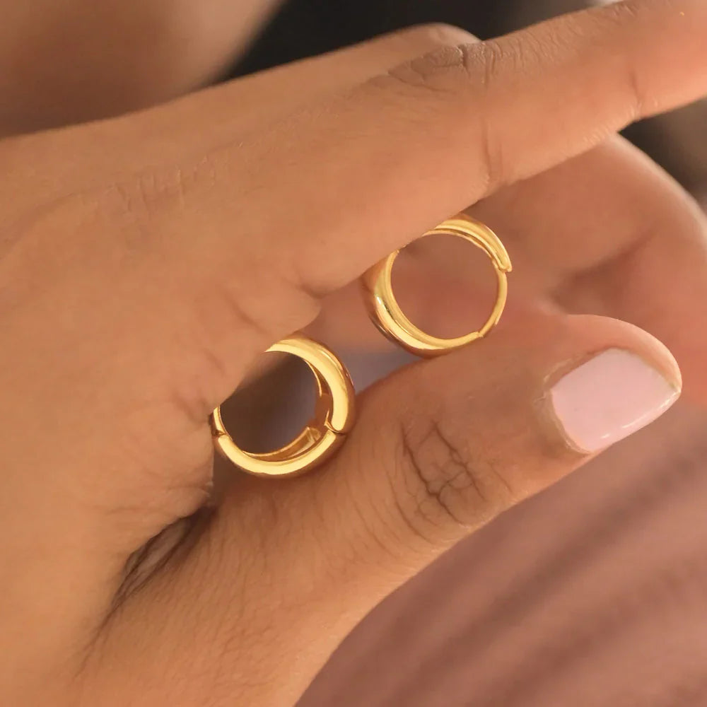 Gold hoop earrings held between fingers with a blurred background