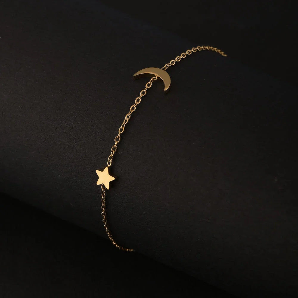 Gold bracelet with star and moon charms on a black background
