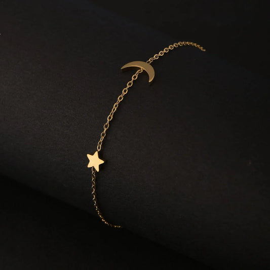 Gold bracelet with star and moon charms on a black background