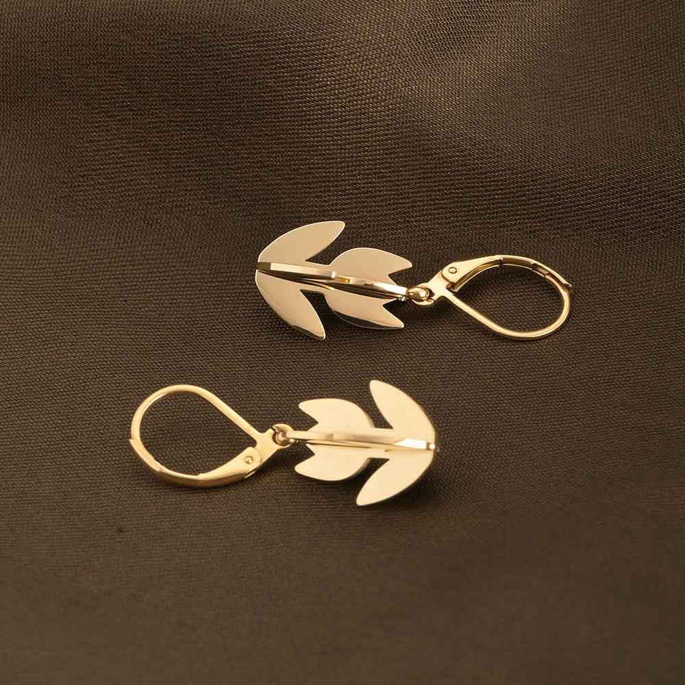 Gold leaf-shaped earrings on a brown background