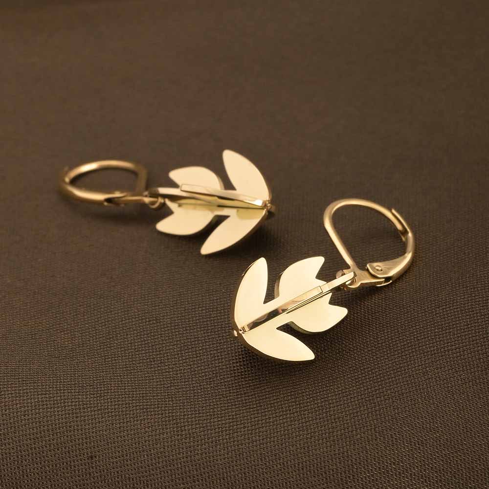 Gold leaf-shaped earrings on a brown background