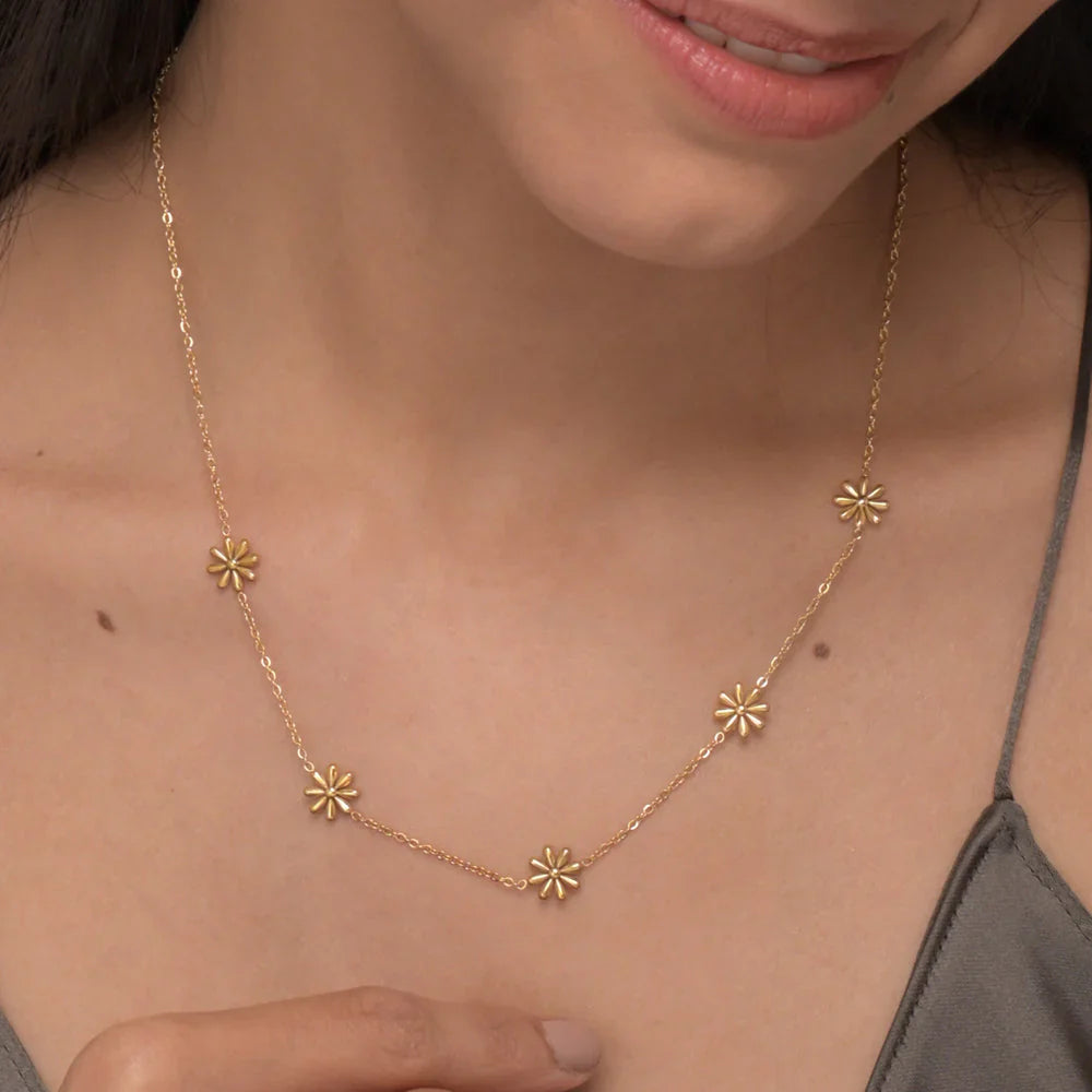 Gold necklace with floral pendants on a person wearing a gray top.